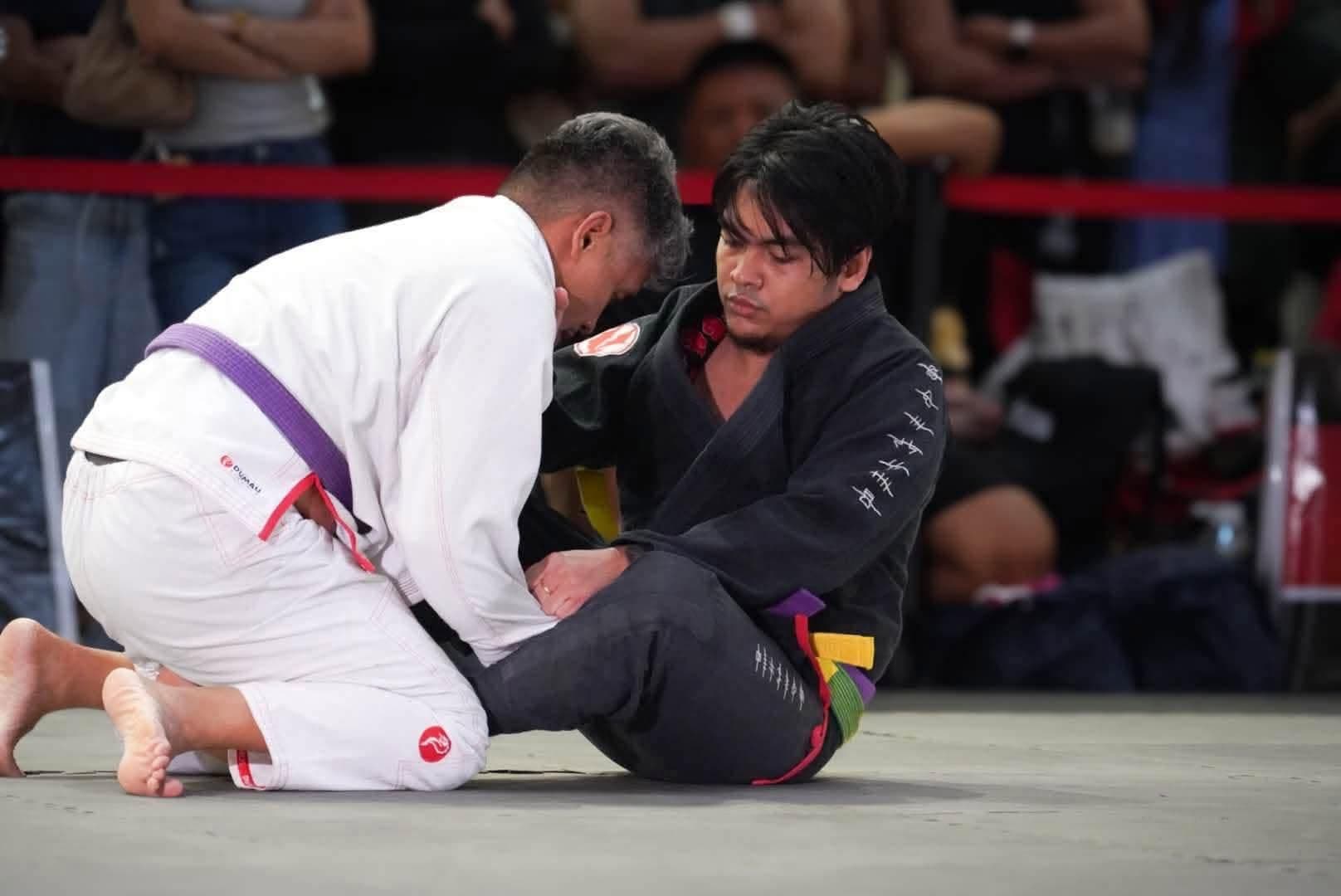 A Kabkad athlete in a black gi playing guard during a jiu jitsu match
